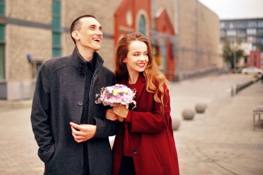 Genç romantik çift, şehirde kalma çiçekler ile güzel kız var. Gri paltolu ve model kırmızı paltolu adam. Mutlu sevgi dolu, gülümseme, bir yürüyüş birlikte Alışveriş Merkezi yakınındaki bir authmn günü zevk.. 