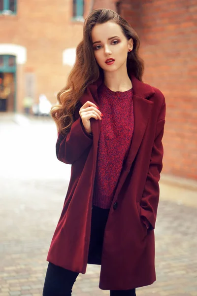 Esmer kız açık havada yaşam tarzı moda portre. Şık kırmızı palto giyiyor. Sokak şehre doğru yürümeye. Uzun kıvırcık saçları hafif. Eğlenceli ve neşeli bir kadın. Sokak moda kavramı. Yüksek moda fotoğraf