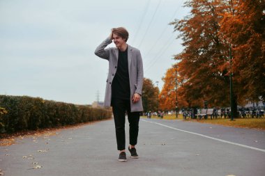 Yakışıklı delikanlı paltolu. Moda iyi giyimli adam şık ceket gülümse. Çocuk sonbahar açık. Mükemmel saç modeli olan zarif adam. Adamın biri park ve gülüyor girer. Sarhoş adamım veya füme gülümseme.