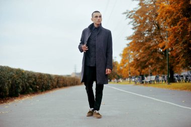 Yakışıklı delikanlı paltolu. Şık ceket poz moda iyi giyimli adam. Kendinden emin ve odaklanmış çocuk sonbahar açık. Mükemmel saç modeli olan zarif adam. İnsan parkta yürüyor.