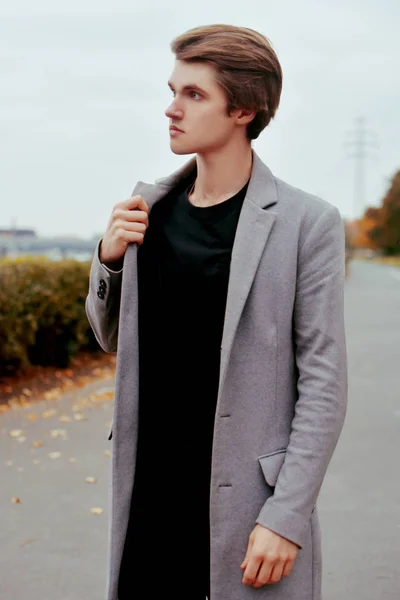 Young handsome man in coat. Portrait of fashionable well dressed man posing in grey stylish coat. Confident and focused boy outdoor at autumn. Elegant man with perfect hairstyle. Male hair styling.