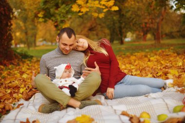 Aşka düşen sonbahar yaprakları bir parkta oturan çift, güzel bir sonbahar günü zevk halıya oturun. Mutlu neşeli genç Aile Baba, anne ve küçük bebek dışarıda eğleniyor.