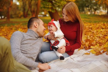 Aşka düşen sonbahar yaprakları bir parkta oturan çift, güzel bir sonbahar günü zevk halıya oturun. Mutlu neşeli genç Aile Baba, anne ve küçük bebek dışarıda eğleniyor.