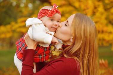 Anne ve kızı bir parkta sonbahar düşen yapraklar üzerinde güzel bir sonbahar günü zevk. Mutlu neşeli genç aile anne açık havada eğleniyor küçük bebeği ile. Uçan Bebek anne öpücüğü