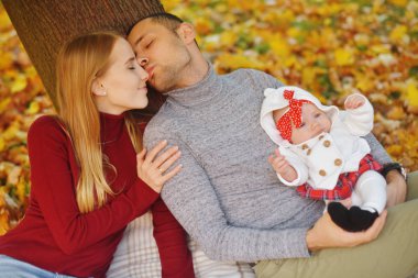 Aşka düşen sonbahar yaprakları bir parkta oturan çift, bir ağacın yanında güzel bir sonbahar günü zevk otur. Mutlu neşeli genç Aile Baba, anne ve bebek kız açık havada eğleniyor.