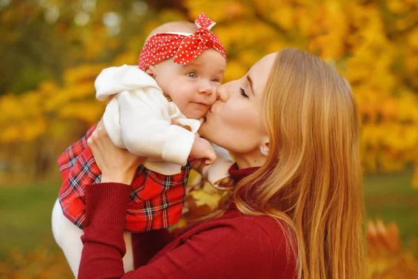Anne ve kızı bir parkta sonbahar düşen yapraklar üzerinde güzel bir sonbahar günü zevk. Mutlu neşeli genç aile anne açık havada eğleniyor küçük bebeği ile. Uçan Bebek anne öpücüğü