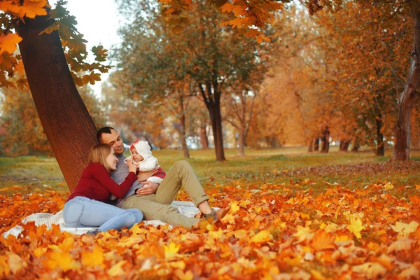 Aşka düşen sonbahar yaprakları bir parkta oturan çift, bir ağacın yanında güzel bir sonbahar günü zevk otur. Mutlu neşeli genç Aile Baba, anne ve bebek kız açık havada eğleniyor.