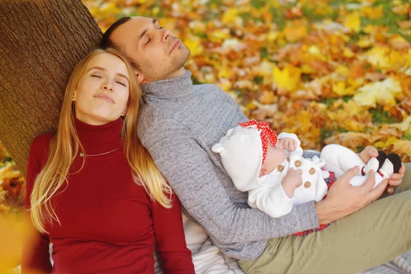 Aşka düşen sonbahar yaprakları bir parkta oturan çift, bir ağacın yanında güzel bir sonbahar günü zevk otur. Mutlu neşeli genç Aile Baba, anne ve bebek kız açık havada eğleniyor.