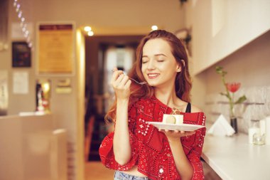 Fırın içindeki kız tatlı yiyor. Bir kafede güzel model tatlılar ve gülümseyen yiyor. Kırmızı kazaklı uzun saçlı güzel kız bir restoran yalnız, diyet yiyor.