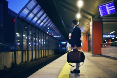 Arka planda tren hareket ile tren istasyonunda kahve olan bir adam duruyor. Bir tren istasyonu platformu üzerinde duran bir beyefendi. iş seyahat, bir tren bekleyen iş adamı.