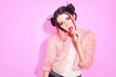 Kız pembe kazanmak buns ile Chupa Chups yiyor. Pembe arka plan üzerinde lolipop yemek oldukça genç bir kızın portresi. Tatlılar yemek hoş gülümseyen genç kız. Sağlık, insan, gıda, diyet.