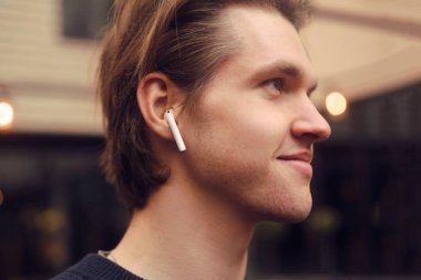 Kablosuz kulaklıklı adam dışarıda, sokakta, restoranda. Adam e-kitap dinliyor, adam müzik dinliyor. Bluetooth kulaklıklı bir adam hayattan zevk alıyor..