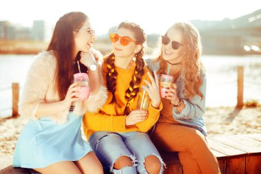 Üç kızlar plaja, nehir, talk, dedikodu, espri, kahkaha, yakın oturmak gülümseme womans gününde. Kızlar sıcak bir gündeki limonata iç. Hipster modeli yaz günü güneş gözlüğü takıyor. Yaz vibes.