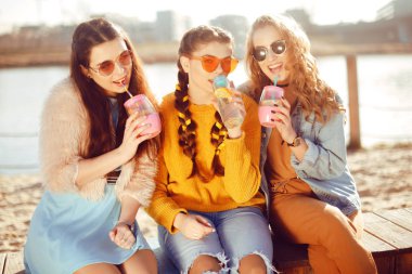 Üç kızlar plaja, nehir, talk, dedikodu, espri, kahkaha, yakın oturmak gülümseme womans gününde. Kızlar sıcak bir gündeki limonata iç. Hipster modeli yaz günü güneş gözlüğü takıyor. Yaz vibes.