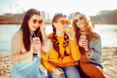 Üç kızlar plaja, nehir, talk, dedikodu, espri, kahkaha, yakın oturmak gülümseme womans gününde. Kızlar sıcak bir gündeki limonata iç. Hipster modeli yaz günü güneş gözlüğü takıyor. Yaz vibes.