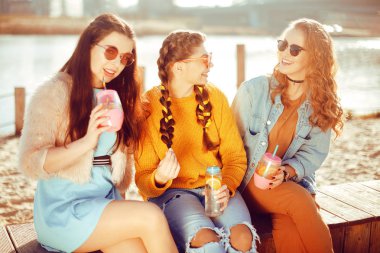 Üç kızlar plaja, nehir, talk, dedikodu, espri, kahkaha, yakın oturmak gülümseme womans gününde. Kızlar sıcak bir gündeki limonata iç. Hipster modeli yaz günü güneş gözlüğü takıyor. Yaz vibes.