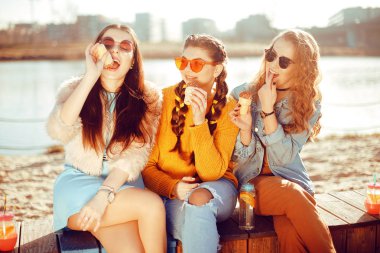 Üç kızlar plaja, nehir, talk, dedikodu, espri, kahkaha, yakın oturmak gülümseme womans gününde. Kızlar sıcak bir günde dondurma yemek. Hipster modeli yaz günü güneş gözlüğü takıyor. Hairslyle kızla