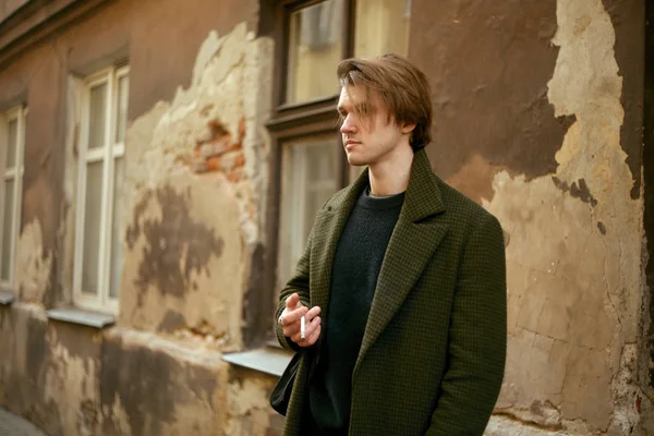 Man on the old street smoking cigarettes, in a long coat. Man befriends a cigarette in the city.  A man like from old movies, vintage.