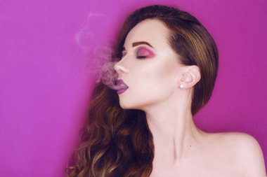 Model kadın yaratıcı renkli pembe ve mavi makyaj. Güzel kızın güzellik portresi. Sigara içen kız, elektronik sigaradan soluyen bir kadının yakın. Mor arka plan