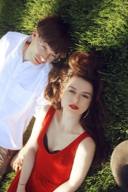 Parkta çimlerin üzerinde yatan romantik bir çift. Mutlu Çift Yeşil Çimenler üzerinde rahatlatıcı. Park. Güzel uzun kırmızı elbiseli bir kız. Kırmızı dudaklı kız. Moda hipster modern çift. Model
