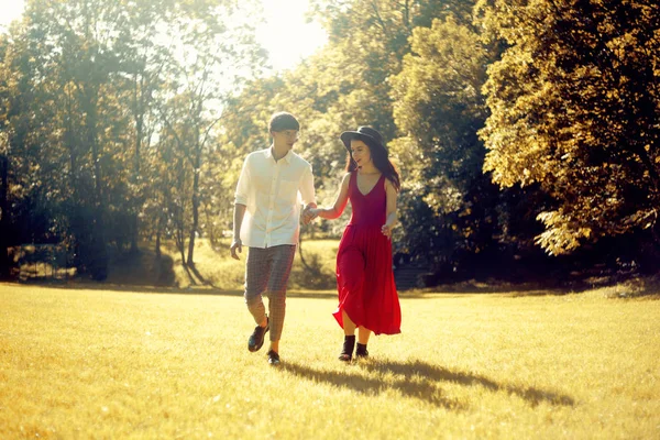 森の中を走るカップル フィールド 長い赤いドレスと帽子の女の子 スタイリッシュな服を着た男 公園の夕焼け 女の子と男が歩く完璧なロマンチックなデート 夏に白いシャツを着た男 — ストック写真