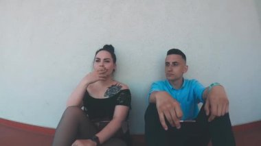 Çift sigara içiyor. Bir kız ve bir erkek kırmızı zeminde oturmuş sigara içiyorlar. Zarar
