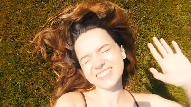 Девушка Лежит Траве Машет Привет Солнечного Города Отдыхает Смотрит Камеру — стоковое видео