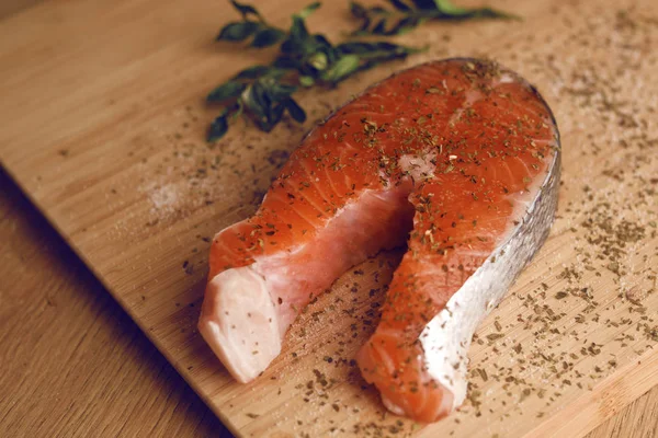 Photo of salmon. Fresh red fish, white veins, rich color. Fish seasoned in spices, dried basil, salt, pepper. Ringfish Fish. Salmon in a wooden plate for cutting basil marinade. Recipe. Fish section.