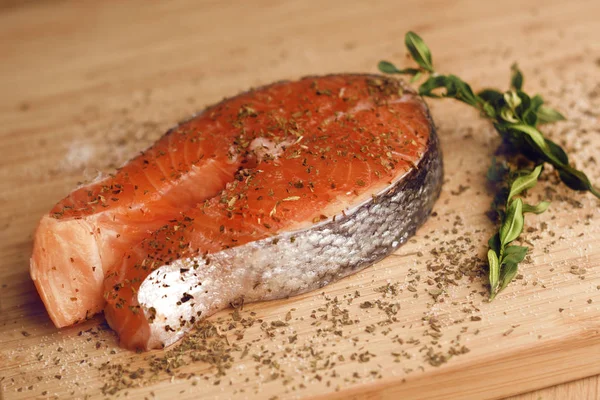 Photo of salmon. Fresh red fish, white veins, rich color. Fish seasoned in spices, dried basil, salt, pepper. Ringfish Fish. Salmon in a wooden plate for cutting basil marinade. Recipe. Fish section.