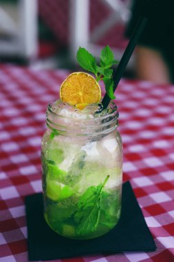 Mojito cam bir kavanoz da hücrede masa örtüsü üzerinde duruyor. Bir restoranda, kafede iç. Karamelize limon, buz, nane, barda güzel bir içki. Hipster içecek servisi.