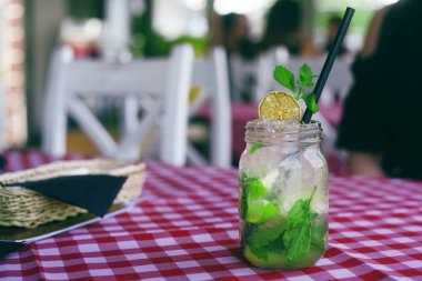 Mojito cam bir kavanoz da hücrede masa örtüsü üzerinde duruyor. Bir restoranda, kafede iç. Karamelize limon, buz, nane, barda güzel bir içki. Hipster içecek servisi.