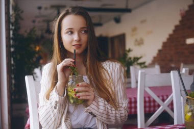 Nehir kenarındaki gemideki bir restoranda bulunan kız mojito içiyor. Esmer gülümsüyor ve bardak kavanozda mojito içiyor. Ceketli uzun saçlı kız, sıcak bir günde mola. İşten sonra kız, öğrenci.