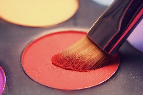 Makeup brush on red shadows. Bright shadows for the summer. Macro frame of shadows. Bright cosmetics, fashionable colors. Bright makeup. Discounts on cosmetics.