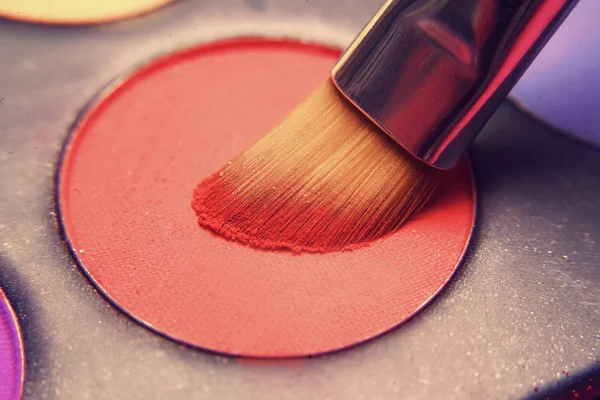 Makeup brush on red shadows. Bright shadows for the summer. Macro frame of shadows. Bright cosmetics, fashionable colors. Bright makeup. Discounts on cosmetics.