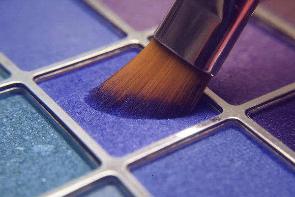 Makeup brush on blue shadows. Bright shadows for the summer. Macro frame of shadows. Bright cosmetics, fashionable colors. Bright makeup. A large palette of bright shadows.