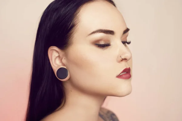 Portrait of a brunette with a tunnel in her ears, and a pierced — Stock Photo, Image