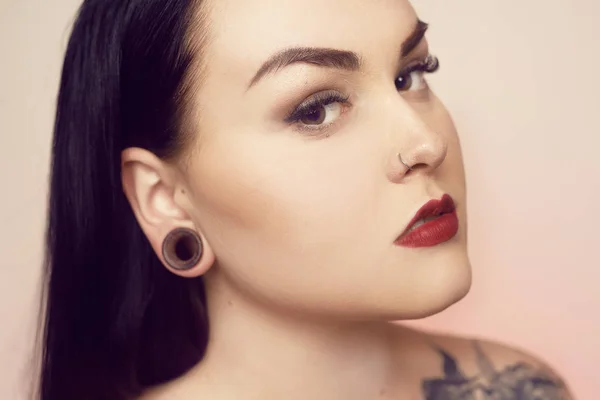 Portrait of a brunette with a tunnel in her ears, and a pierced — Stock Photo, Image