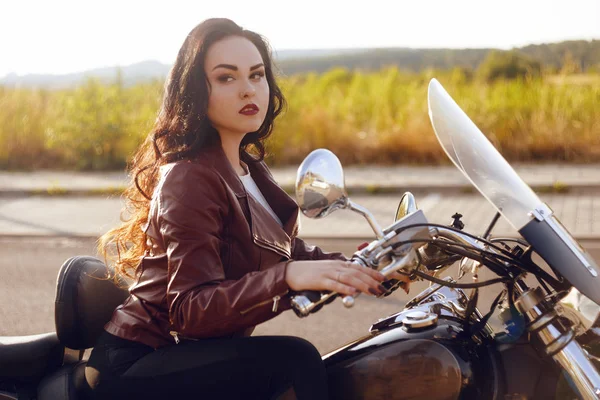 Beautiful brunette in a red leather jacket on a motorcycle in th — Stock Photo, Image