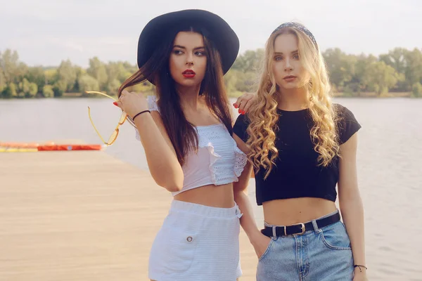 Duas meninas na moda, amigos, ficar no cais perto do rio — Fotografia de Stock