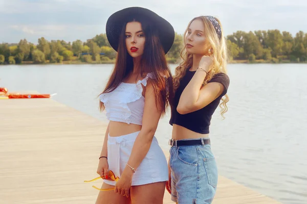 Zwei modische Freundinnen stehen auf der Seebrücke am Fluss — Stockfoto