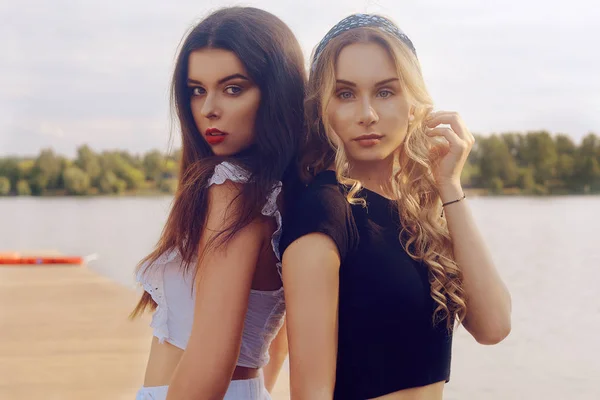 Duas meninas na moda, amigos, ficar no cais perto do rio — Fotografia de Stock