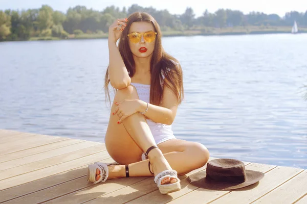 Das Mädchen sitzt auf der Seebrücke in der Nähe von Fluss, See und Strand. brünette — Stockfoto