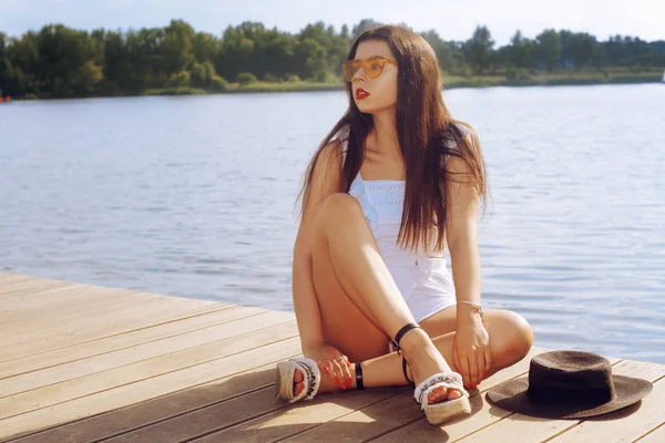 Flickan sitter på piren nära floden, sjön, stranden. Brunett — Stockfoto
