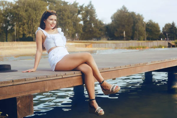 Dziewczyna siedzi na molo w pobliżu rzeki, jeziora, plaży. Brunetka — Zdjęcie stockowe
