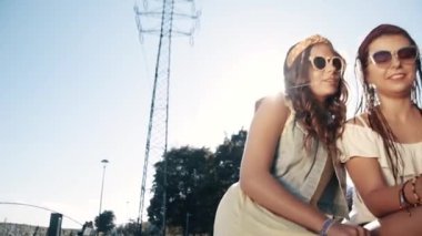 İki kız arkadaş / kız kardeş bir şezlongda oturup internette sohbet ediyorlar, kız arkadaşlar bir erkekle sohbet ediyorlar, telefona bak, tartış, gül, flört sitesi. Kızlar dedikodu yapar. İki güzel esmer