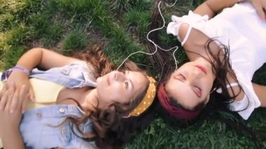 İki kız / kız kardeş çim üzerinde, kulaklık müzik dinliyor yatıyor. İki esmer parkta çimenlerin üzerinde uzanır, rahatlar, şarkı söylerler..