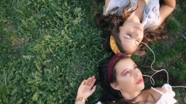 İki kız / kız kardeş çim üzerinde, kulaklık müzik dinliyor yatıyor. İki esmer parkta çimenlerin üzerinde uzanır, rahatlar, şarkı söylerler..