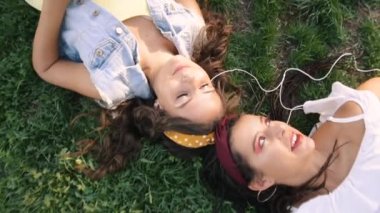 İki kız / kız kardeş çim üzerinde, kulaklık müzik dinliyor yatıyor. İki esmer parkta çimenlerin üzerinde uzanır, rahatlar, şarkı söylerler..