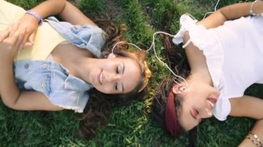 İki kız / kız kardeş çim üzerinde, kulaklık müzik dinliyor yatıyor. İki esmer parkta çimenlerin üzerinde uzanır, rahatlar, şarkı söylerler..
