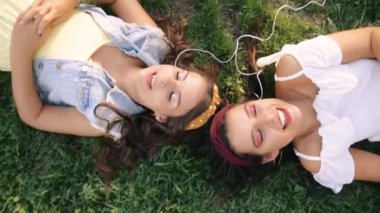 İki kız / kız kardeş çim üzerinde, kulaklık müzik dinliyor yatıyor. İki esmer parkta çimenlerin üzerinde uzanır, rahatlar, şarkı söylerler..
